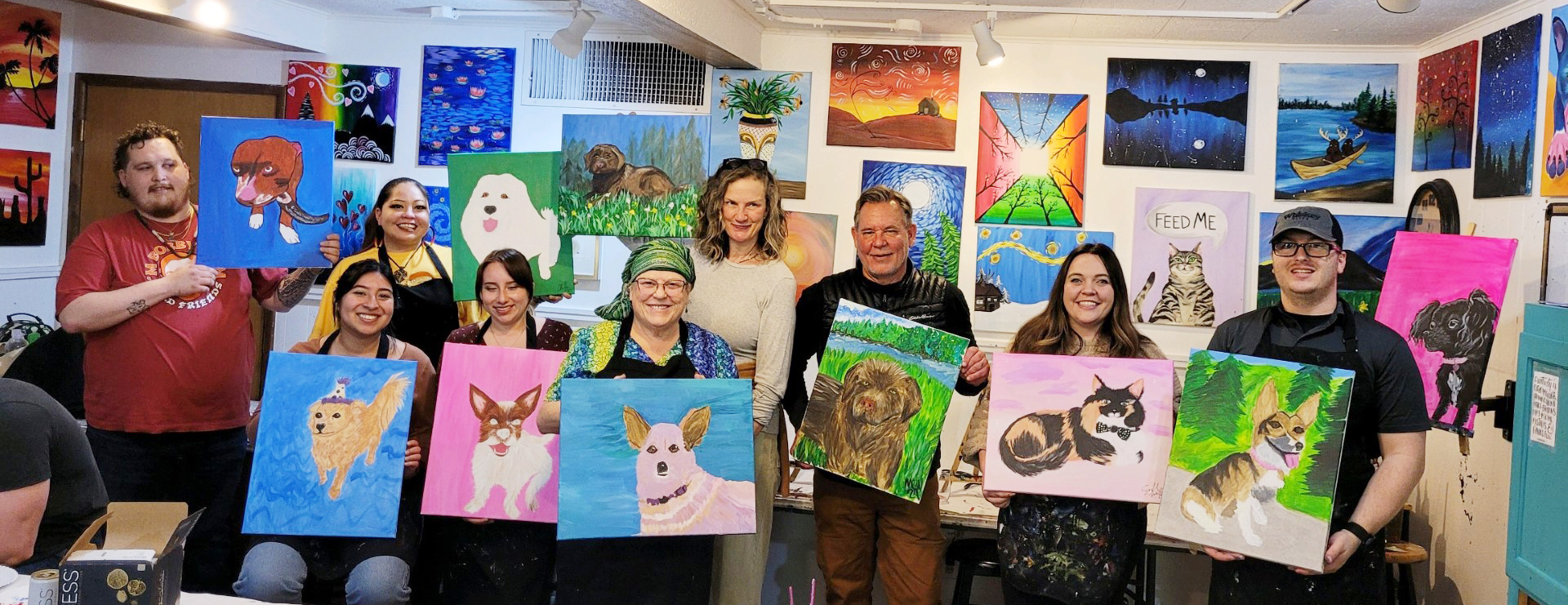 A group of people holding up paintings in front of a wall.